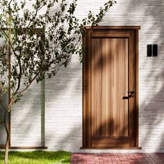 a wooden door sitting next to a white brick wall near a tree and potted plant