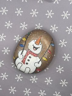 a painted rock with a snowman holding a lite - up candle and wearing a party hat