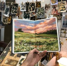 a person holding an open book in front of a wall with pictures and paintings on it