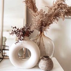 two vases with dried plants in them sitting on a table next to a mirror