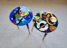 two colorful painted stools sitting on top of a white carpet next to each other