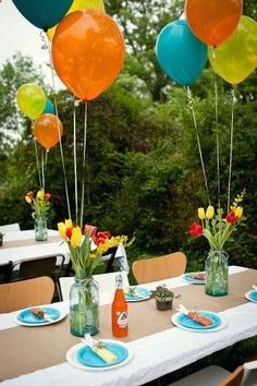 the table is set for an outdoor party with balloons and flowers in vases on it