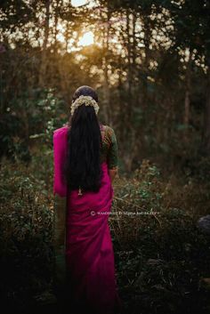 a woman standing in the woods with her back turned to the camera, wearing a pink sari