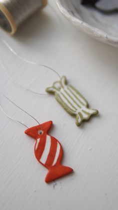 two red and white fish ornaments on a table next to a spool of thread