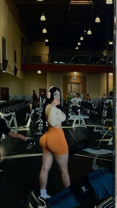 a woman in an orange short and white shirt is walking through a gym with other people