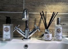 a bathroom sink with soap, reeds and lotion bottles next to the faucet