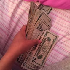 a person is laying on a bed with some money in their hand and the sheets are pink