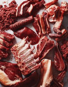 various cuts of meat on a cutting board with red stuff all over the place and around them