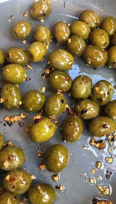 some green olives are sitting in a pan on the stove top, with seasoning sprinkled around them