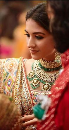 a woman in a red and gold sari is looking at something on her hand