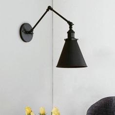 a black wall light next to a vase with yellow flowers on it and a chair in the background