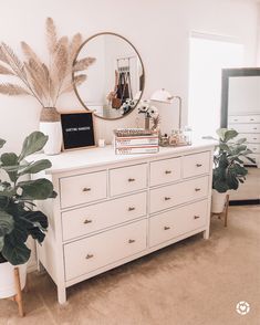 a white dresser and mirror in a room with plants on the top shelf, potted plant next to it