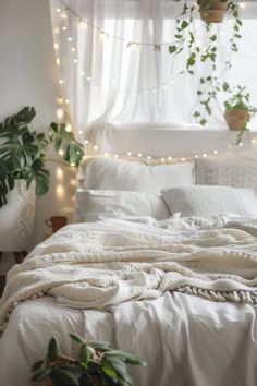 an unmade bed with white sheets and blankets on top of it, surrounded by potted plants