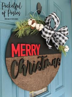 a wooden merry christmas sign hanging on a blue door with a black and white bow