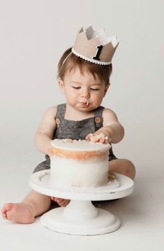 a baby sitting on the floor with a cake in front of him and wearing a crown