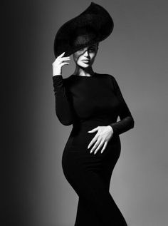 a woman in a black dress and hat poses for a fashion magazine photo shoot with her hands on her hips