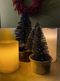 two small christmas trees sitting on top of a wooden table next to a lit candle