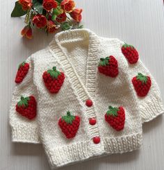 a knitted cardigan with strawberries on the front and back, sitting next to a bouquet of flowers