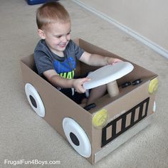 a young boy sitting in a cardboard box with a white frisbee on it