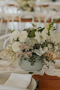 a table with white flowers and greenery in a silver vase on top of it