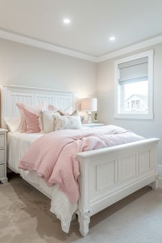 a white bed with pink comforter and pillows in a large room next to a window