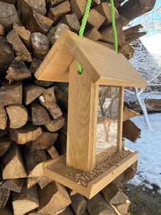 a wooden bird feeder hanging from a rope on top of wood stacked in front of a pile of logs