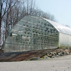 a green house sitting on top of a dirt field next to trees and rocks in front of it