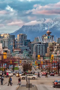 people crossing the street in front of tall buildings with snow capped mountains in the background