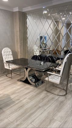 a glass dining table with white chairs in front of a mirrored wall and mirror behind it