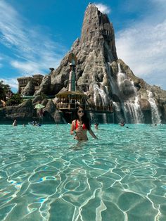 a woman standing in the middle of a pool next to a waterfall and water slide