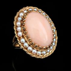 Step into a world of vintage charm with this mic last century substantial cocktail ring, crafted in gleaming 14k yellow gold. A smooth, large oval angelskin coral cabochon sits at the heart of this piece, framed by embellished gold prongs that elevate its presence like a beautiful frame. Surrounding the coral, a halo of lustrous pearls strung on gold wirework lends a touch of classic elegance. The ring's face is bordered by a twisted rope design, adding textural contrast and intricate detail. Supported by a robust triple split shank, this ring makes a bold yet sophisticated statement, perfectly capturing the 1940s dedication to craft and opulence Metals: 14k gold Markings: 14k hallmark Gemstones: coral - cabochon oval cut coral approximately 19x14.5mm, seed pearls Ring Size: 6.75 Total Wei High Luster Vintage Ring Jewelry, Classic Oval Ring With High Luster, Classic Oval Rings With High Luster, Classic Oval High Luster Ring, Vintage Yellow Gold Oval Cabochon Jewelry, High Luster Oval Ring In 14k Gold, High Luster 14k Gold Oval Rings, Luxury Round Jewelry For Vintage Events, Oval Heirloom Jewelry For Collectors