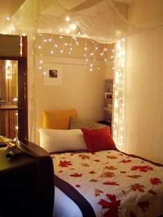 a bedroom with lights strung from the ceiling and a bed covered in white sheets, red and yellow pillows