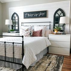 a bedroom with white walls and black iron bed frame, pillows, and throw pillows