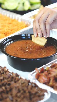 a person dipping cheese into a bowl of soup in front of other food on the table