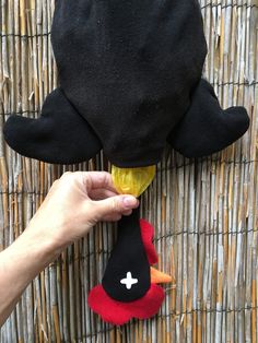 a hand holding a stuffed animal on top of a woven mat next to a bamboo fence