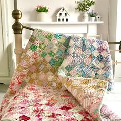 a bed with a quilt on top of it next to a white shelf and potted plant