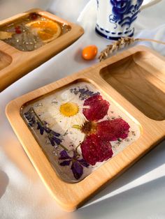 two wooden trays with flowers on them sitting on a white tablecloth covered table