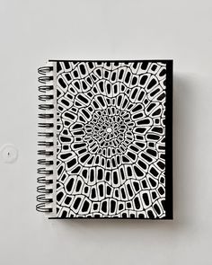 a spiral notebook with an intricate design on the front and back cover, sitting on top of a white surface