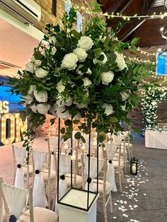 white flowers and greenery are on display in the middle of rows of chairs at an event