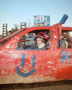 a young boy sitting in the driver's seat of an old red race car