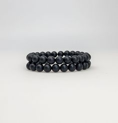 "DETAILS:  8mm matte black onyx beaded bracelet on clear elastic stretch cord. A smooth matte finish gives the bracelet a sleek modern look.  It is a minimalist-style unisex stretch bracelet making it a good choice for men, women, and teens.  It can be worn on its own or stacked with other bracelets for a trendy layered look. The stretchy design allows for easy comfortable wear, making it the perfect fit for anyone. It also makes a thoughtful gift for a loved one who appreciates unique and meani Classic Black Bracelets With 8mm Beads, Adjustable Black Bracelets With 8mm Beads, Adjustable Black Wristband With 8mm Beads, Adjustable Black Wristband With Round Beads, Minimalist Black Stretch Bracelet With Round Beads, Minimalist Black Wristband With Round Beads, Classic Adjustable Black Wristband, Adjustable Black Hand-strung Stretch Bracelet, Adjustable Hand-strung Black Stretch Bracelet