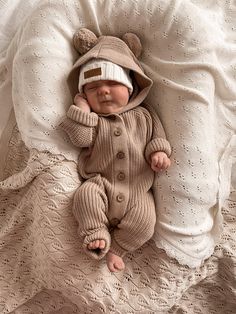 a baby is laying down on a bed wearing a knitted bear suit and hat