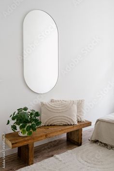 a white room with a wooden bench, mirror and potted plant on the floor