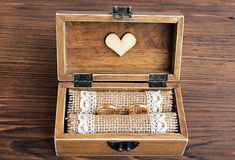 an open wooden box with two wedding rings inside on top of a table next to a pair of glasses