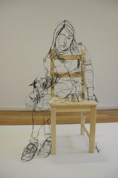 a wooden chair sitting on top of a white floor next to a drawing of a woman