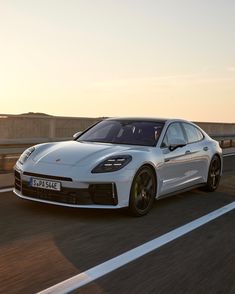 a white porsche panamera driving down the road at sunset or dawn with its lights on