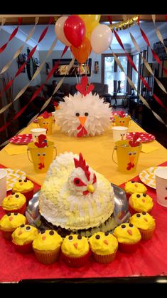 a table topped with cupcakes covered in frosting next to a chicken cake