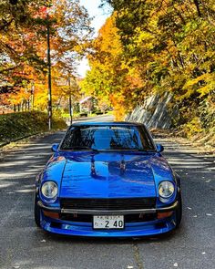 a blue car parked on the side of a road in front of trees with fall colors