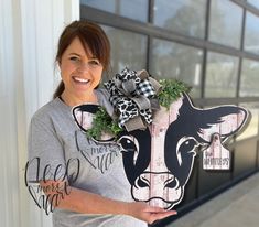 a woman holding up a cow sign with greenery on it's head and wearing a t - shirt