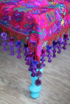 a colorful table cloth with tassels and beads on the legs is sitting on a wooden floor